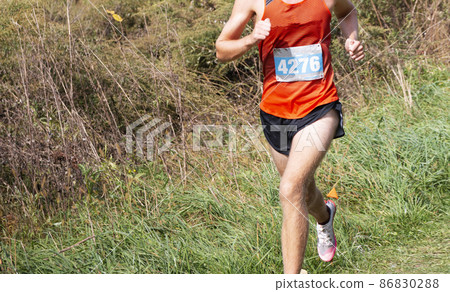 Runner running a race on a grass field downhill 86830288
