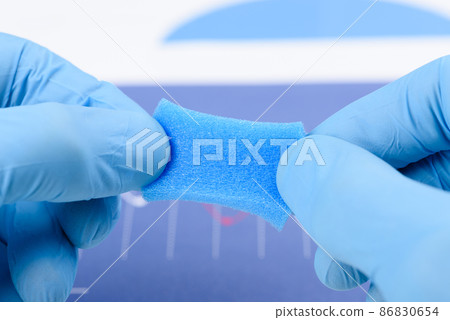 Blue porous sponge like material stretched in scientist hands in laboratory.  86830654
