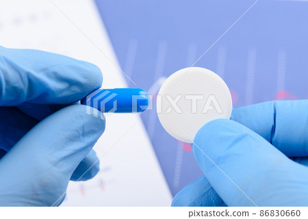 Scientist hold in hands and compare big carbon effervescent pill and small blue capsule 86830660