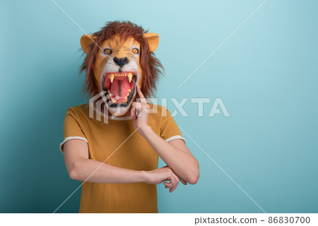 Young woman in lion mask with hand on chin, thinking, pensive expression, isolated on blue   86830700