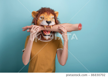 Young woman in lion mask with bitten off hand in her mouth, isolated on blue background. Young woman in lion mask with bitten off hand in her mouth, isolated on blue background. 86830702