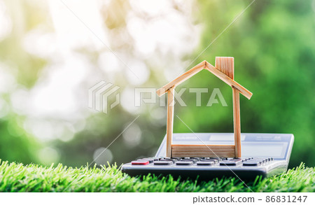 House is on the calculator placed on the grass. Imagine calculating to buy a home. planning savings money of coins to buy a home House is on the calculator placed on the grass. Imagine calculating to buy a home. planning savings money of coins to buy a home 86831247