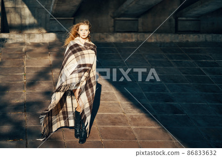 Full length portrait of pretty young woman wrapped in blanket posing ib sun lights over urban background 86833632