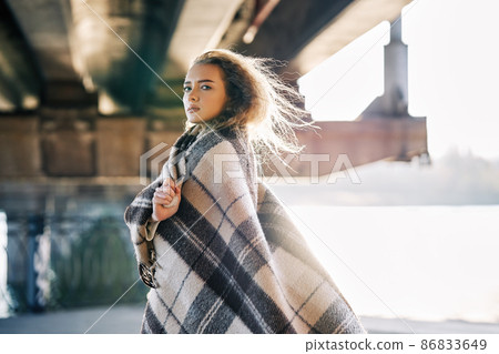 Portrait of pretty confident woman wrapped in wool blanket looking to camera posing on urban street background with copy space Portrait of pretty confident woman wrapped in wool blanket looking to camera posing on urban street background with copy space 86833649