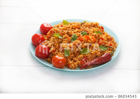 Jollof rice, tomatoes and hot peppers on a blue plate on a white background. National cuisine of Africa. Jollof rice, tomatoes and hot peppers on a blue plate on a white background. National cuisine of Africa. 86834543
