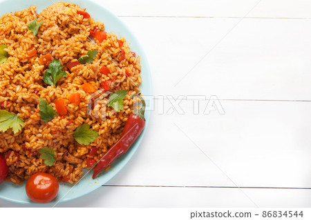 Jollof rice, tomatoes and hot peppers on a blue plate on a white background. National cuisine of Africa. Copy spaes. 86834544