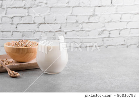 Vegan non diary buckwheat milk in glass on a wooden plate with buckwheat groats on a grey table. Veggies healthy milk 86836798