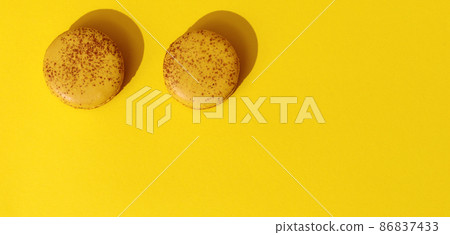 Two Yellow french macaroons on bright yellow and white background. Delicious meringue cookies. Food concept Two Yellow french macaroons on bright yellow and white background. Delicious meringue cookies. Food concept 86837433