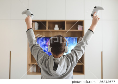 Boy in headphones watching television, teenager boy playing video game in front of screen at home Boy in headphones watching television, teenager boy playing video game in front of screen at home 86838677