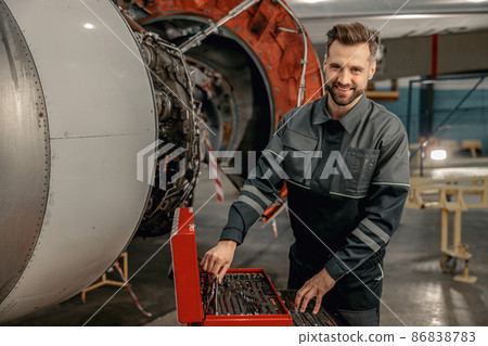 Cheerful man aircraft mechanic using tool box in hangar 86838783