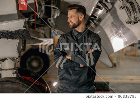 Cheerful male mechanic standing near aircraft in hangar Cheerful male mechanic standing near aircraft in hangar 86838785