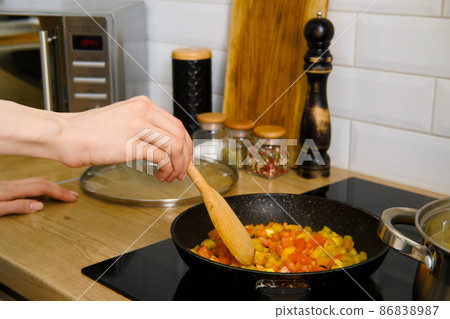 Closeup view of female hand stirring chopped vegetables in a frying pan with wooden spatula 86838987