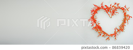 Arranged heart symbol of ruscus branches with red leaves on bright background in panoramic frame. Arranged heart symbol of ruscus branches with red leaves on bright background in panoramic frame. 86839420