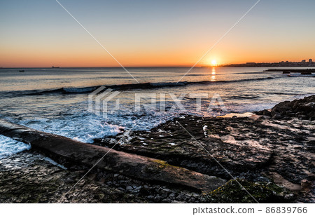 Rocky beach with small waves and a colorful sunset at the Atlantic Ocean in Estoril 86839766