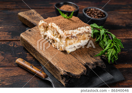 Italian dessert Tiramisu cake with cocoa and mint on a wooden board. Dark Wooden background. Top view 86840046
