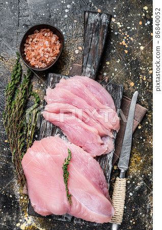 Sliced Raw turkey breast fillet meat on a cutting board with butcher knife. Brown background. Top View 86840052