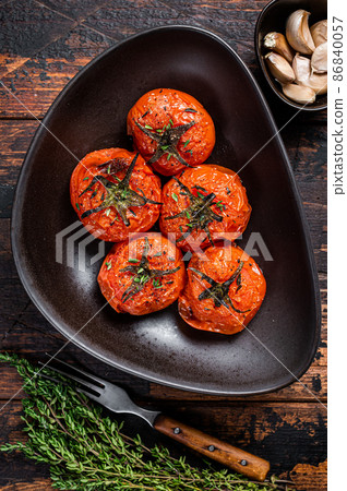 Oven Roasted cherry tomatoes with thyme and garlic in a plate. Dark wooden background. Top view Oven Roasted cherry tomatoes with thyme and garlic in a plate. Dark wooden background. Top view 86840057