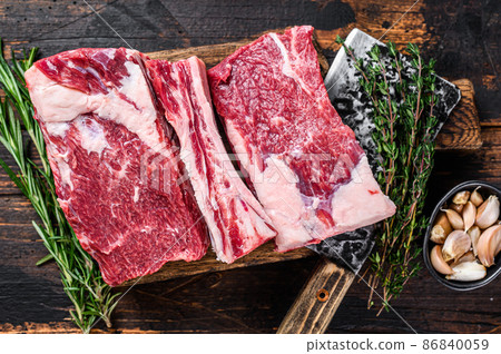 Raw beef calf short ribs meat on a butcher cutting board with cleaver. Dark wooden background. Top view 86840059