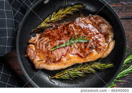 Grilled striploin beef meat steak in a pan with herbs. Dark wooden background. Top view Grilled striploin beef meat steak in a pan with herbs. Dark wooden background. Top view 86840060