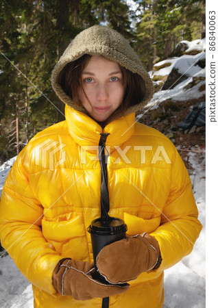 caucasian woman in a jacket and mittens holding a paper cup, coniferous forest caucasian woman in a jacket and mittens holding a paper cup, coniferous forest 86840063