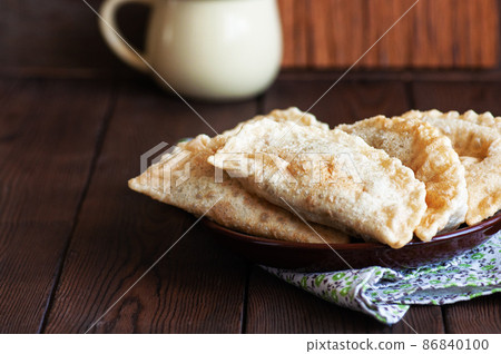 Freshly fried empanadas or chebureki with meat served on a plate. Wooden background. Freshly fried empanadas or chebureki with meat served on a plate. Wooden background. 86840100