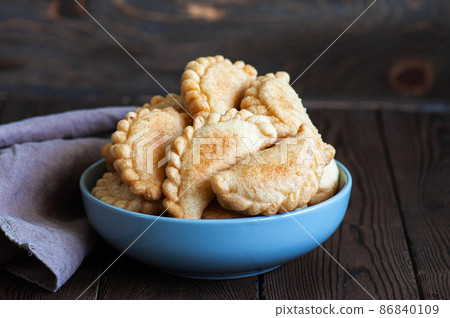 Freshly fried hand pies with meat in a bowl on a wooden background. Close up. 86840109