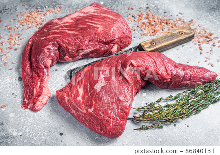 Unccoked tri-tip triangle roast, raw bottom sirloin steak on buther table with meat cleaver. Gray background. Top view Unccoked tri-tip triangle roast, raw bottom sirloin steak on buther table with meat cleaver. Gray background. Top view 86840131