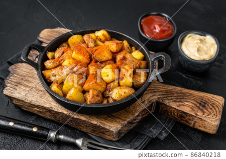 Patatas bravas, spicy potatoes, a Spanish dish with fried potato and a spicy garlic sauce. Black background. Top view Patatas bravas, spicy potatoes, a Spanish dish with fried potato and a spicy garlic sauce. Black background. Top view 86840218