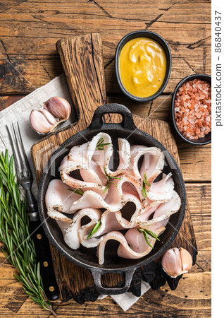 Fresh sliced lard with salt, garlic and pepper in pan with herbs. Wooden background. Top view 86840437