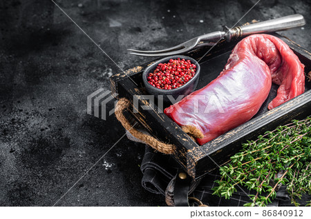 Whole raw veal beef tenderloin in wooden tray. Black background. Top view. Copy space 86840912