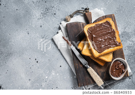 Toast with chocolate Hazelnut spread on wooden board. Gray background. Top view. Copy space Toast with chocolate Hazelnut spread on wooden board. Gray background. Top view. Copy space 86840933