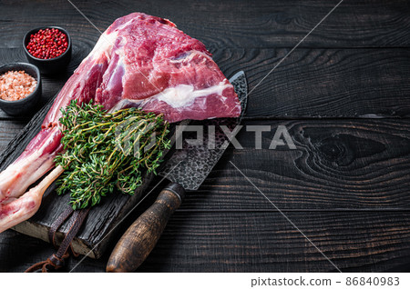 Uncooked Raw lamb mutton leg with herbs on butcher cutting board. Black wooden background. Top view. Copy space Uncooked Raw lamb mutton leg with herbs on butcher cutting board. Black wooden background. Top view. Copy space 86840983
