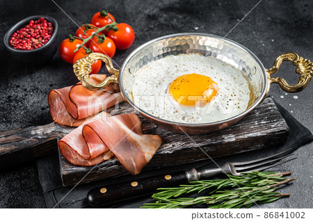 Breakfast with fried egg in a skilet with tomatoes and bacon. Black background. Top view Breakfast with fried egg in a skilet with tomatoes and bacon. Black background. Top view 86841002