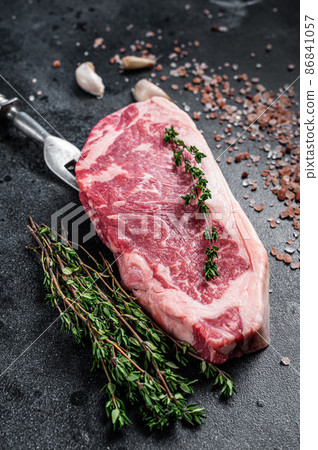 Raw new york strip steak on a butcher table with salt and thyme. Black background. Top view Raw new york strip steak on a butcher table with salt and thyme. Black background. Top view 86841057