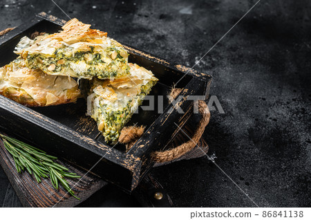 Spinach pie pieces, Spanakopita Greek Pie in wooden tray. Black background. Top view. Copy space Spinach pie pieces, Spanakopita Greek Pie in wooden tray. Black background. Top view. Copy space 86841138