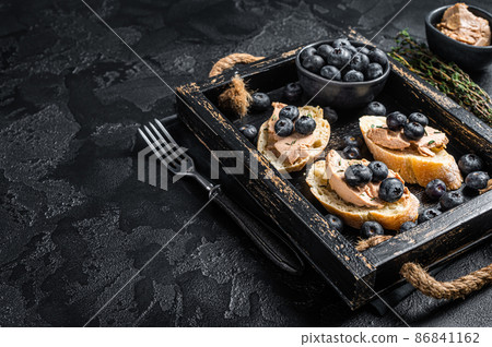 Foie gras toasts, duck liver pate and fresh blueberry in wooden tray. Black background. Top view. Copy space 86841162