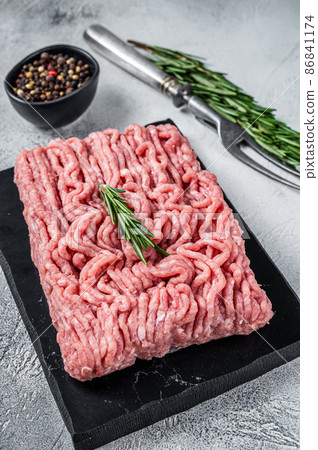 Minced chicken or turkey raw meat on cutting board with herbs. White background. Top View 86841174