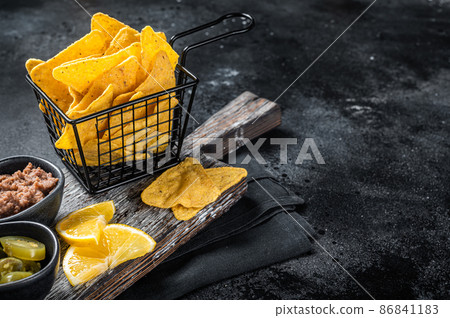 Mexican nachos corn chips with Chili con carne and jalapeno in a basket. Black background. Top view. Copy space Mexican nachos corn chips with Chili con carne and jalapeno in a basket. Black background. Top view. Copy space 86841183