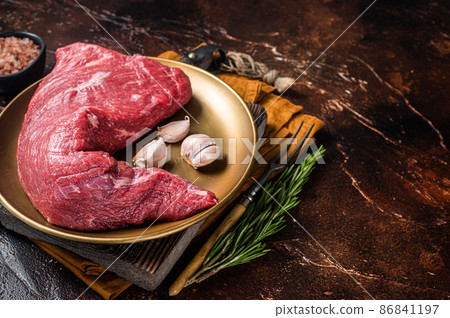 Raw tri-tip triangle roast or bottom sirloin steak on plate with herbs. Dark background. Top view. Copy space 86841197