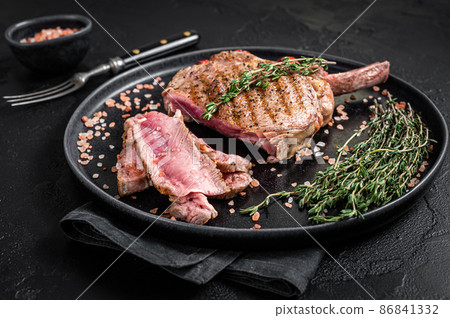 Barbecue sliced rib eye Tomahawk beef (veal) steak on a plate with pink salt. Black background. Top view 86841332