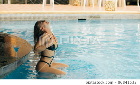 The pretty woman drinking blue cocktail alcohol liquor and sit at the bar. Cocktail bar in the swimming pool. Portrait of sexy girl in pool outdoor. 86841532