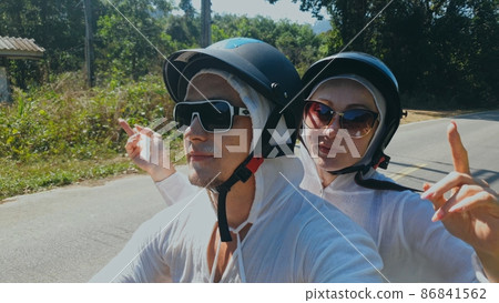 Two caucasian tourist woman man drive on red scooter. Make it selfie. Love couple on motorbike in white clothes to go on forest road trail trip. Two caucasian tourist woman man drive on red scooter. Make it selfie. Love couple on motorbike in white clothes to go on forest road trail trip. 86841562
