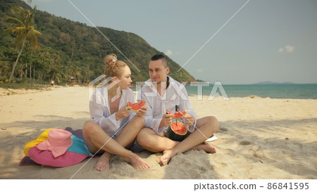 The cheerful love couple holding and eating slices of watermelon on tropical sand beach sea. Romantic lovers two people spend summer weekend. The cheerful love couple holding and eating slices of watermelon on tropical sand beach sea. Romantic lovers two people spend summer weekend. 86841595