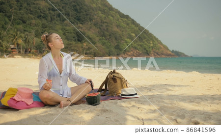 The cheerful woman in holding and eating slices of watermelon on tropical sand beach sea. Portrait attractive girl spend summer weekend. The cheerful woman in holding and eating slices of watermelon on tropical sand beach sea. Portrait attractive girl spend summer weekend. 86841596