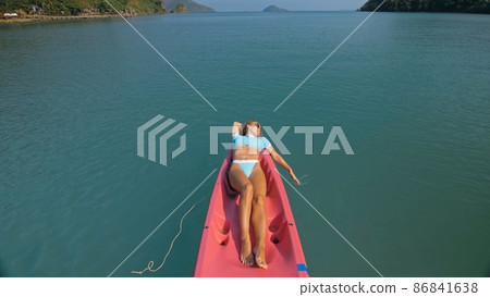 Pretty slim woman in elegant swimsuit lies in pink plastic kayak drifting on azure ocean at exotic resort upper view. 86841638