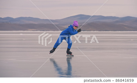 The child train on ice professional speed skating. The girl skates in the winter in sportswear, sport glasses, suit. Outdoor slow motion. 86841659