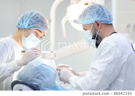 Surgeon and nurse during a dental operation. Anesthetized patient in the operating room. Installation of dental implants in the clinic. Surgeon and nurse during a dental operation. Anesthetized patient in the operating room. Installation of dental implants in the clinic. 86842193