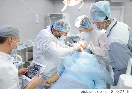 Surgeons and nurse during a dental operation. Medical team performing surgical dentistry operation. Anesthetized patient in the operating room. Installation of dental implants in the clinic. 86842236
