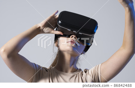 Young brunette woman wearing a virtual reality headset goggles and playing a game with a friends in metaverse. Future technology concept. Young brunette woman wearing a virtual reality headset goggles and playing a game with a friends in metaverse. Future technology concept. 86842488