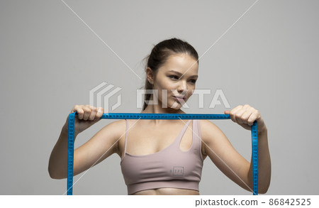 Sexy attractive brunette female in sportswear outfit holding a blue measuring tape in front of her face. Weight loss and diet concepts. Health care and healthy nutrition. Perfect slim body. Sexy attractive brunette female in sportswear outfit holding a blue measuring tape in front of her face. Weight loss and diet concepts. Health care and healthy nutrition. Perfect slim body. 86842525